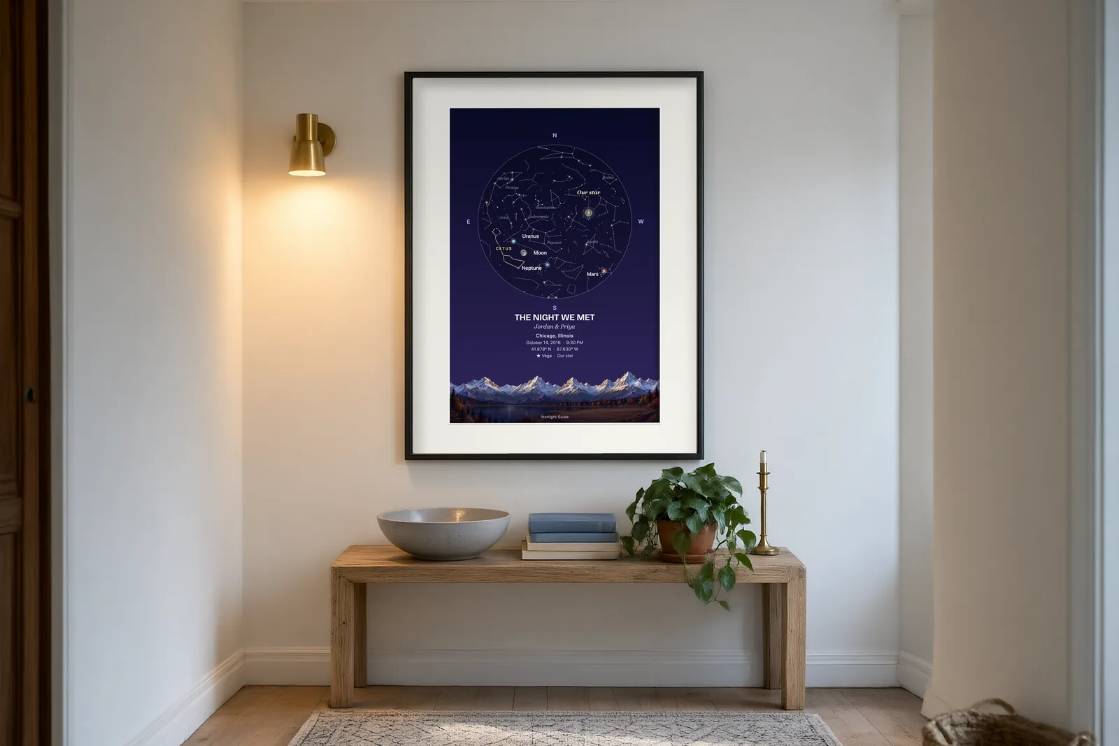 A star map with a painted mountain horizon, framed in a hallway lit by a warm wall sconce.
