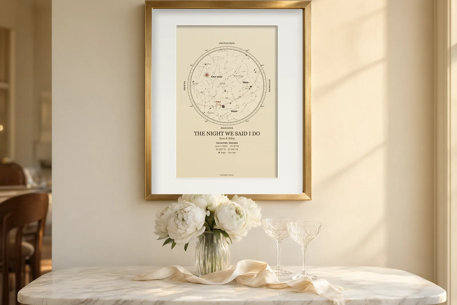 A cream star map titled 'The Night We Said I Do' in a gold frame above a marble console with white peonies and champagne glasses.